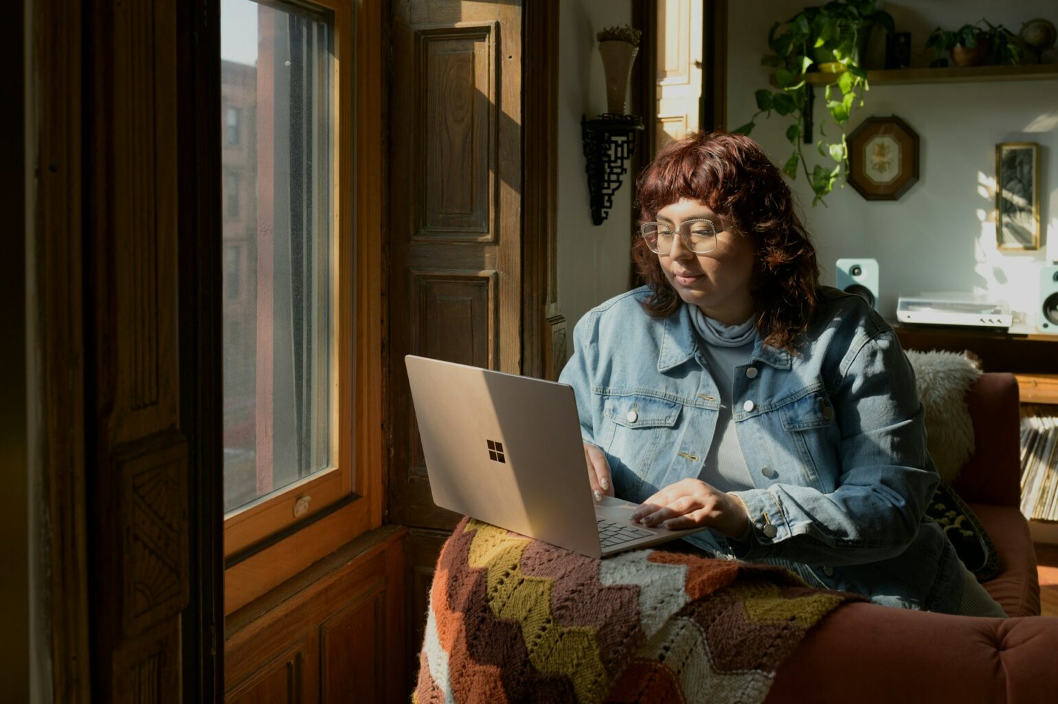 La fotografía muestra a una mujer trabajando en su Chromebook sentada cerca de la ventana de un dormitorio.