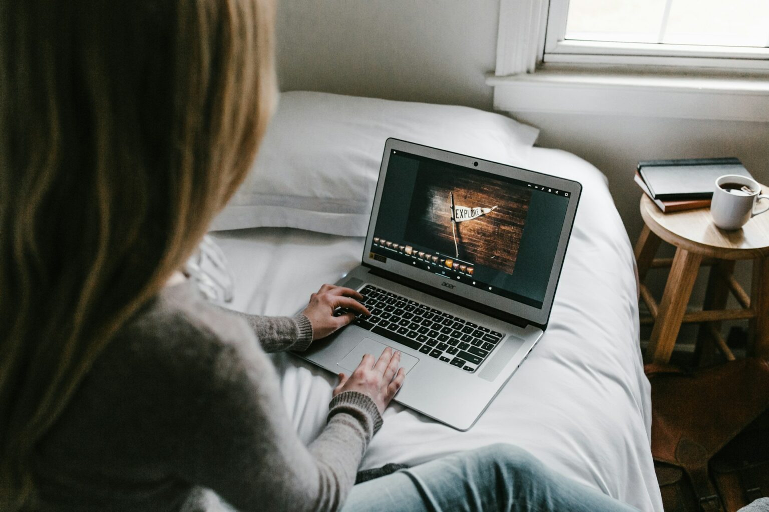 La fotografía muestra a una mujer de espaldas trabajando en su Chromebook sobre su cama.