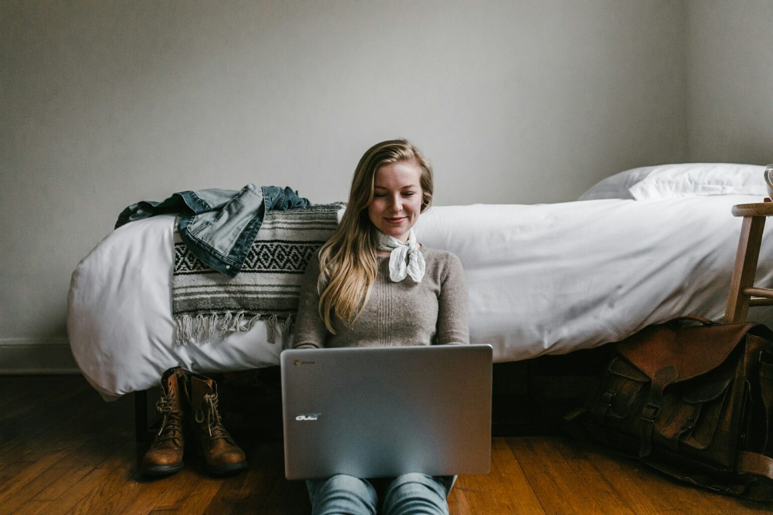 La fotografía muestra a una mujer trabajando en su Chromebook sentada en el suelo de su dormitorio.